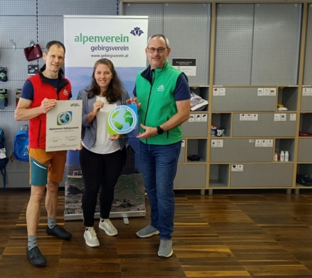 Zwei Männer und eine Frau stehen in einem Raum mit Kletterausrüstung und halten die Klimabündnis-Tafeln in der Hand.