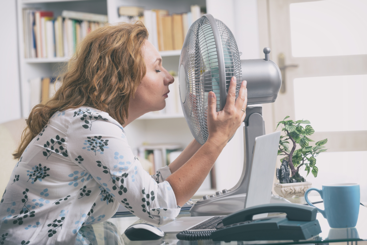Woman suffers from heat while working in the office and tries to cool off by the fan