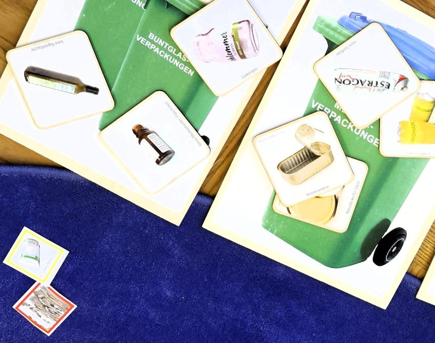 Kartonkarten mit Abbildung von Mülltonnen und kleineren Chips mit Abbidungen von verschiedenem Müll aus Karton