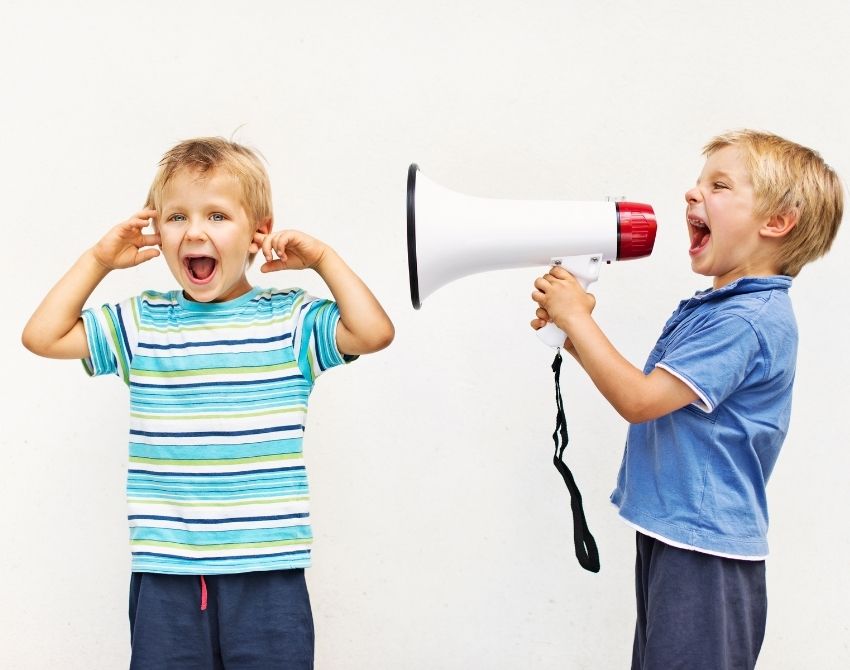kind mit megaphon schreit anderem kind ins ohr, welches sich die ohren zuhält