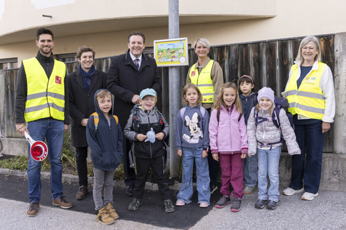 Kinder und Erwachsene, teils mit Signalwesten, stehen an einem Pedibus-Stop